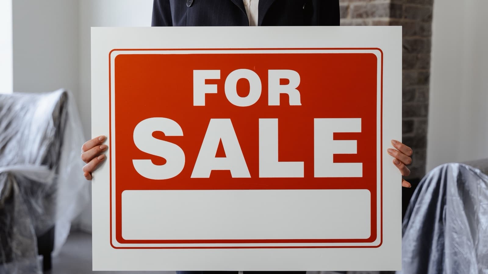 A person holding a red and white For Sale sign inside a home